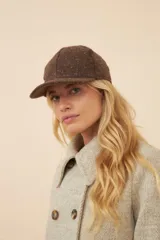 Gorra con visera confeccionada en lana fina sin teñir, con un sutil patrón de tejido en espiga.