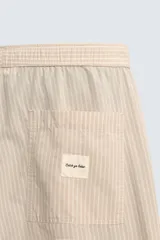 Pantalón relaxed fit color beige con rayas verticales finas, confeccionado en tejido de algodón. Cuenta con cintura elástica ajustable con cordón, bolsillos frontales y bolsillos traseros de plastrón.