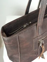 Bolso tipo shopper de cuero marrón chocolate, con doble asa de hombro, cierre superior y bolsillo frontal con cierre y tirador decorativo de cuero con estampa animal print.