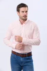 Camisa Oxford lisa de color rosado, con cuello abotonado, cierre frontal de botones, manga larga con puños ajustables y un bolsillo aplicado en el pecho.