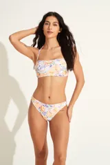 Top de bikini bandeau con estampado de flores y frutas en tonos blanco, naranja, violeta y verde. Tiene un tirante fino al cuello.