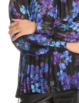 Blusa de gasa plisada con estampado floral en tonos azules y violetas sobre fondo negro. Presenta cuello alto, mangas largas con puños abotonados y un diseño fluido con textura plisada.