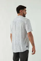 Camisa de manga corta con cuello cubano, confeccionada en viscosa con estampado de hojas en tonos azules. Presenta cierre frontal abotonado y corte slim.