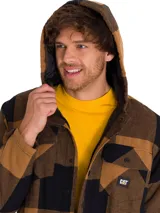 Chaqueta tipo camisa de franela con capucha, diseño a cuadros en tonos marrón y negro. Cuenta con cierre frontal a presión, bolsillos en el pecho con solapa y bolsillos laterales. Incluye logo de la marca en el bolsillo izquierdo.