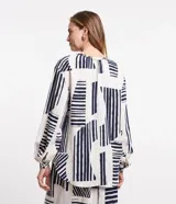 Camisa amplia de viscolino con estampado geométrico en azul marino sobre fondo crudo. Tiene cuello redondo con lazo, mangas largas abullonadas y abotonadura frontal.