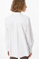 Camisa blanca de corte clásico con cuello camisero y cierre frontal de botones. Presenta un bordado lineal en color marrón oscuro en ambos lados del frente, representando motivos florales.