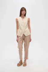 Chaleco color beige claro, sin mangas, con escote en V profundo y cierre frontal asimétrico con botones.