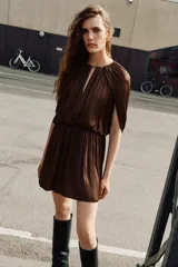 Vestido corto de tejido satinado color marrón, con cuello redondo, mangas largas con diseño fluido y cintura elástica. Presenta una abertura frontal y cierre posterior con botón.