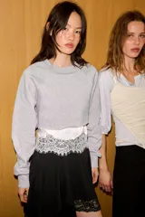 Sudadera crop de cuello redondo y manga larga con puños elásticos. Presenta un diseño de doble capa con un top interior satinado y un bajo decorado con encaje a tono.