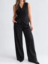 Conjunto de dos piezas compuesto por chaleco cruzado sin mangas con cinturón lateral y pantalón de pierna ancha, en color negro.