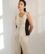 Chaleco sin mangas de lino, con diseño de paneles en color blanco crudo y beige. Presenta escote redondo y cierre frontal con botones de madera marrones.