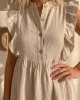 Vestido corto de lino color beige, sin mangas con volados en los hombros, cuello mao con botones frontales de nácar, corte en la cintura fruncido y falda con volado en el ruedo.