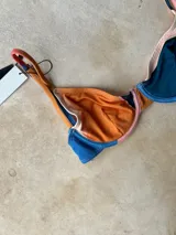 Top de bikini con aro, diseño de bloques de color en tonos azul, naranja y crema, con breteles regulables y cierre metálico en la espalda.