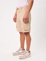 Bermuda cargo de gabardina color beige, con bolsillos laterales con fuelle en las piernas, bolsillos delanteros tipo ojal y traseros. Cuenta con presillas para cinto y cierre frontal con botón y cierre.