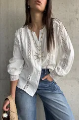 Camisa blanca de manga larga con detalles de encaje y diseño abotonado en la parte delantera.