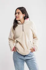 Buzo de sherpa color crema con cierre parcial con cremallera, cuello alto y bolsillos laterales.