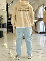 Canguro oversize color beige, con capucha y amplio estampado tipográfico en la espalda.
