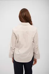 Camisa de corte clásico con cuello camisero, cierre frontal de botones y bolsillo en el pecho. Presenta un diseño de rayas verticales finas en tonos beige y blanco.