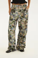 Pantalón de tiro medio de denim con estampado floral multicolor en tonos verdes, azules y naranjas, de corte wide leg y piernas amplias.