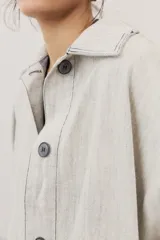 Chaqueta oversize de gabardina color verde claro, con solapa clásica, bolsillos frontales, cierre de botones oscuros y mangas largas con vuelta en tono verde lima vibrante.