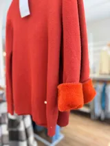 Polera de cuello alto en color terracota, confeccionada con un interior suave y cálido. Presenta puños y ruedo acanalados, con un pequeño aplique metálico decorativo en la parte inferior.
