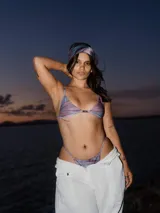Top de bikini triangular con estampado tie-dye en tonos violeta, azul y rosa. Tiene breteles finos y un detalle metálico en el centro del busto.