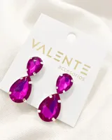 Aros colgantes con dos piedras sintéticas en forma de lágrima color fucsia, engarzadas en metal plateado.