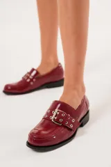 Mocasines color rojo charol con hebilla metálica y ojalillos.