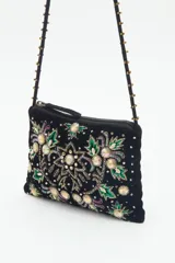 Cartera de mano o bandolera pequeña de terciopelo negro con bordado floral multicolor y apliques de lentejuelas y cuentas brillantes. Correa delgada negra con tachas doradas.