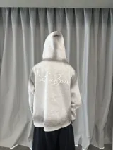 Buzo con capucha y cierre frontal, color gris con efecto lavado degradado. Presenta estampado gráfico en color blanco que recorre el pecho y las mangas, bolsillos laterales y etiqueta de marca en el puño.