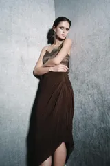 Falda midi marrón oscuro, confeccionada en tejido plisado con detalle de drapeado lateral y bajo asimétrico.