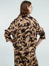 Camisa de manga larga con estampado abstracto en tonos beige y negro, con botones delanteros y bolsillos en el pecho.
