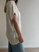 Blusa blanca de corte relajado, con escote en V, mangas cortas amplias y detalles de bordados florales en relieve.