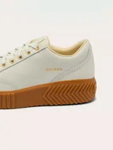 Zapatillas Sorel modelo Ona Ave Low, de diseño minimalista en color crema con suela de plataforma dentada en tono caramelo. Presenta cierre de cordones con ojales metálicos dorados y logo de la marca grabado en el lateral.