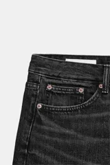 Bermuda de tiro medio confeccionada en denim de color negro gastado, con diseño de cinco bolsillos, trabillas para cinturón y cierre frontal con cremallera y botón metálico.