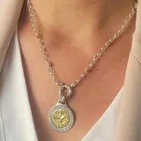 Conjunto compuesto por una cadena de eslabones redondos en plata y un dije circular con diseño de grecas en el borde y figura central en oro.