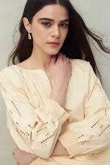 Blusa de algodón color crema o amarillo pálido, con escote en V y mangas largas con detalle de bordado calado (broderie) con motivos florales y frunce elástico en los puños.