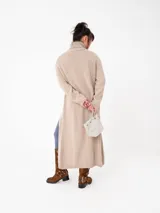 Buzo largo gris de tejido de punto grueso con cuello alto y capucha con orejas de conejo rojas. Tiene mangas largas y un tajo lateral.