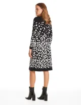 Vestido midi de tejido de punto con diseño integrado que simula un conjunto de vestido y cárdigan. Presenta un color base negro con detalles geométricos en blanco en las mangas y el ruedo. Posee escote redondo y mangas largas.