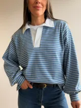 Buzo tipo chomba de corte oversize con diseño a rayas horizontales celestes y blancas. Presenta cuello camisero blanco y un bordado en la espalda con la inscripción República Oriental del Uruguay.