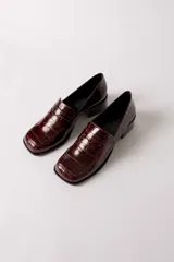 Mocasín de cuero con textura de reptil en color bordó, con puntera cuadrada y taco bloque bajo de color negro.