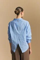 Camisa de manga larga a rayas verticales blancas y azules, con cuello camisero, cartera frontal con botones y calce relajado.