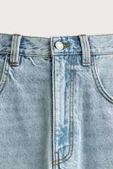 Bermuda de denim de algodón con efecto lavado desgastado en tonos marrones y azules. Tiene tiro medio, diseño de cinco bolsillos, pierna recta de corte holgado y bajo con acabado irregular. Cuenta con cierre frontal de cremallera y botón metálico.