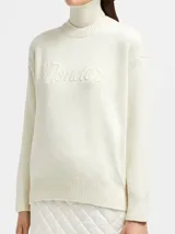 Buzo de lana y cachemira color crema, con cuello alto y logo de la marca bordado en el frente.