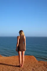 Vestido corto negro de punto smock, sin mangas, con cuello alto y detalle de volado en el ruedo.