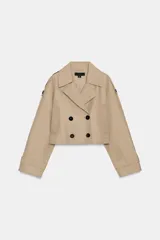 Trench corto de color beige con cuello de solapa, cierre frontal cruzado con botones y mangas largas con trabillas ajustables en los puños. Presenta un diseño estructurado con hombreras y bolsillos delanteros de vivo.