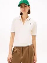 Chomba de piqué color blanco de Tommy Hilfiger, con mezcla de algodón elástico y lyocell. Presenta manga corta, cuello camisero con cierre frontal de cremallera y detalles de líneas oscuras en cuello, puños y dobladillo. Incluye logo bordado en el pecho.