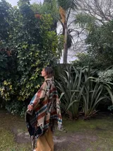 Poncho estilo navajo confeccionado en mezcla de lana y algodón, con estampado geométrico multicolor en tonos beige, marrón, negro, turquesa y blanco, y terminación de flecos en el ruedo.