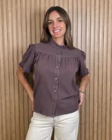 Camisa de manga corta color marrón con cuello alto con volados, botonadura frontal y detalles de costuras a contratono.