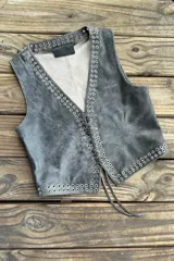 Chaleco negro de cuero con escote en V y cierre frontal con cordones. Presenta ojalillos metálicos plateados a lo largo de los bordes.